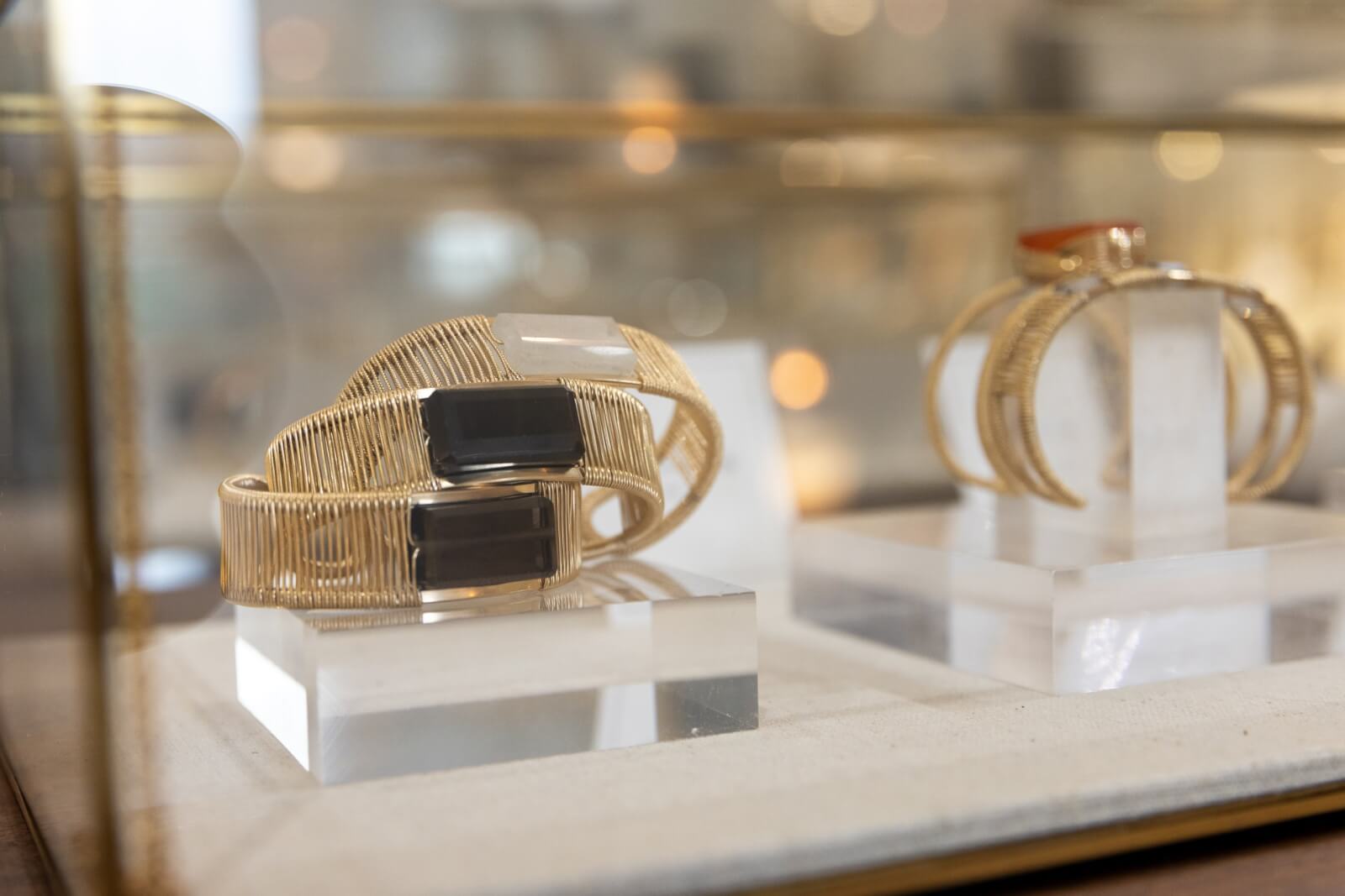 Two exquisite gold bracelets with striking black rectangular stones by Judith Bright are displayed on white platforms in a glass case.