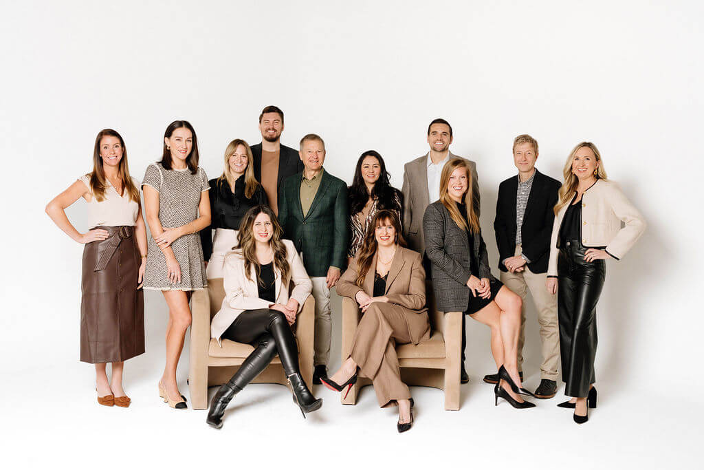 A group of eleven professionally dressed people, representing The CityLiving Group at Village, pose together against a plain white background, with some standing and others seated on two chairs.