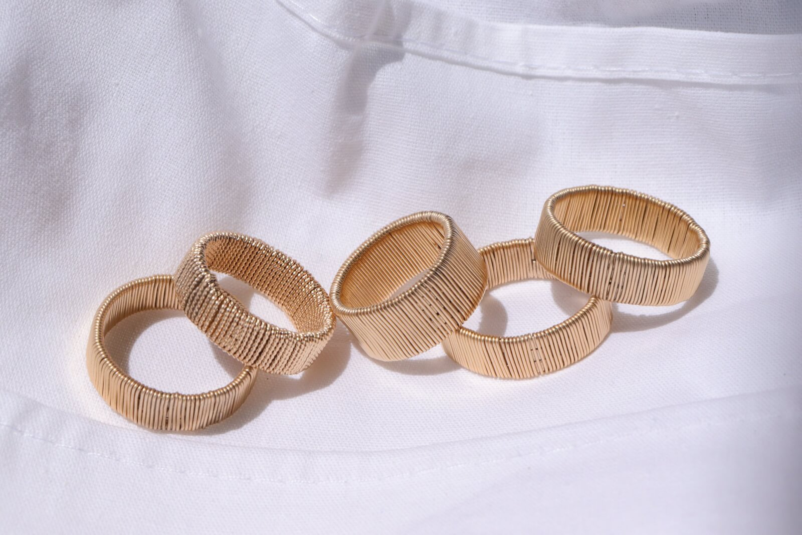 Five exquisite gold-tone textured rings by Judith Bright are arranged on a white fabric surface, their intricate designs slightly overlapping in a harmonious pattern.