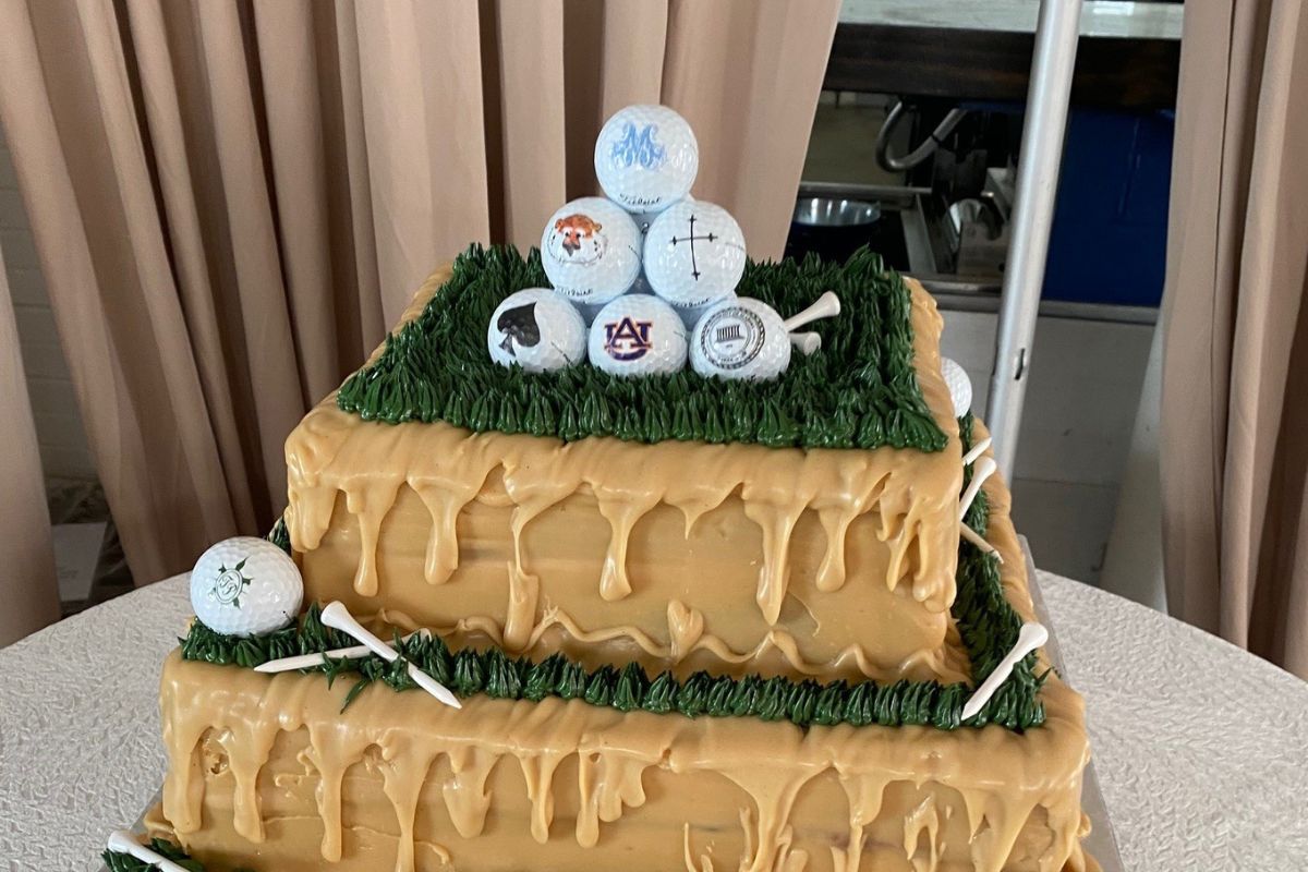 A two-tiered cake with caramel icing and green grass frosting, featuring dessert designs of a pyramid of golf balls and golf tees.