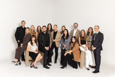 A group of fifteen professionally dressed people from The CityLiving Group at Village pose together against a plain white background, some standing and others seated on chairs.