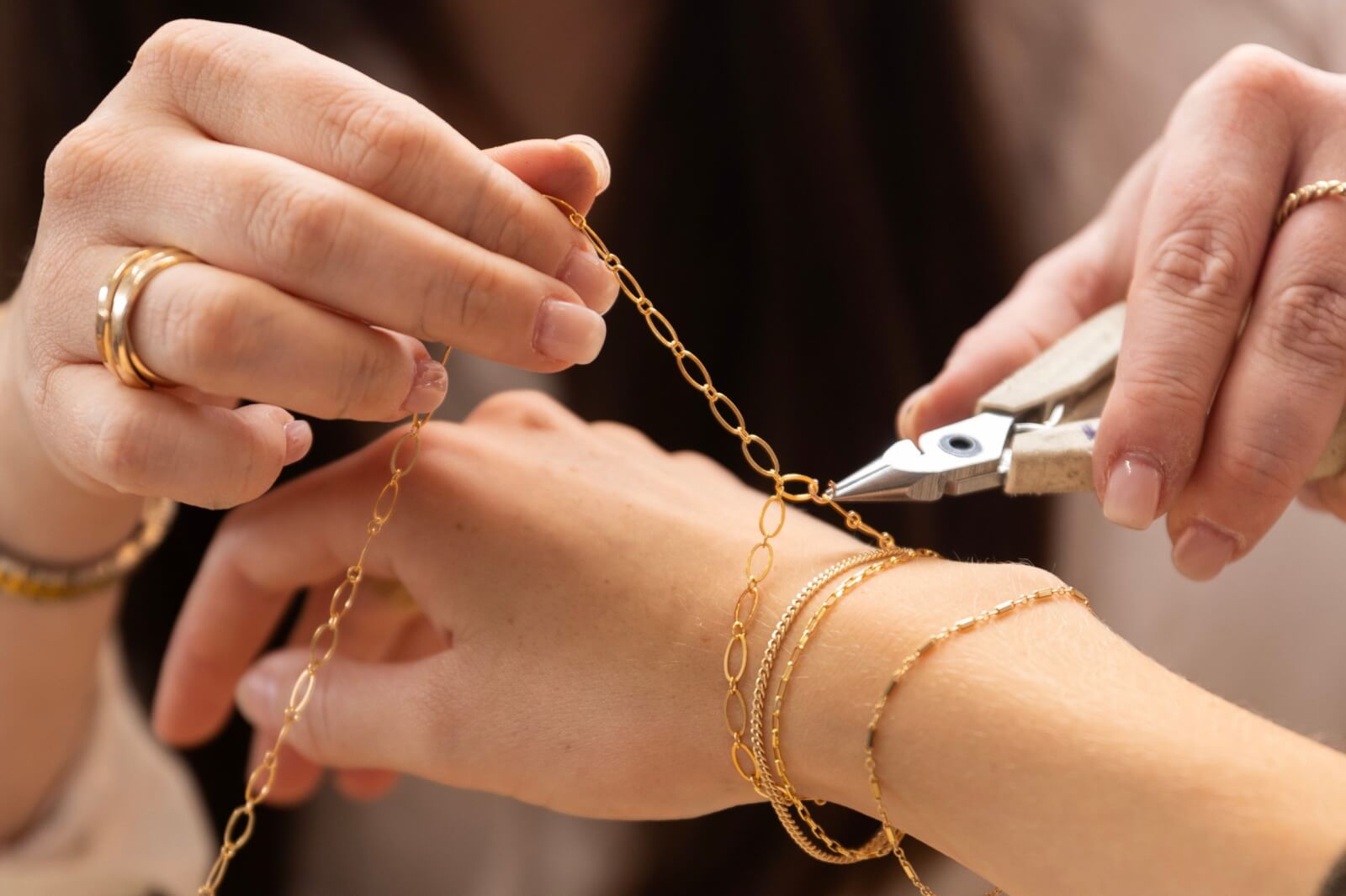 A person uses pliers to adjust a Judith Bright gold chain bracelet on another person's wrist, showcasing the delicate craftsmanship and elegance of the designer's piece.