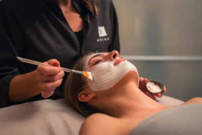 An aesthetician at Escape Day Spa and Salon uses a brush to apply a white facial mask to a woman lying down.