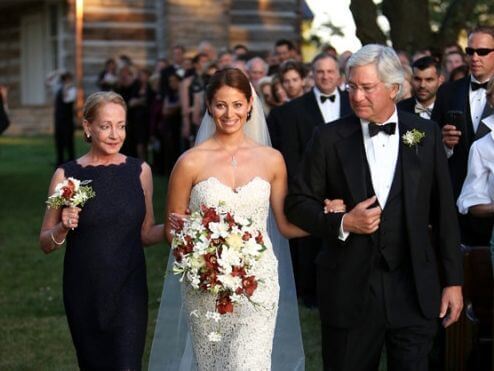 The bride's parents escort her down the path with friends and family cheering them on.