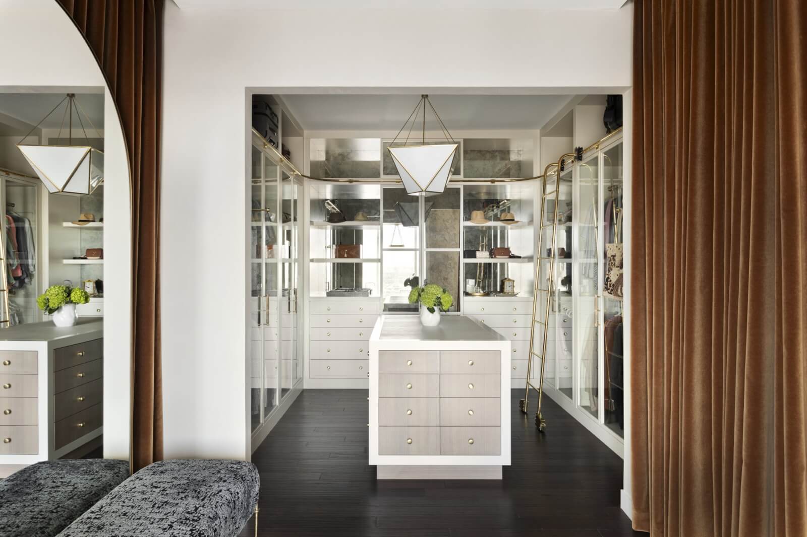 Spacious, modern walk-in closet by Providence Interiors featuring a central island, glass-panel cabinets, sleek lighting, and brown curtains—a true masterpiece of interior design.