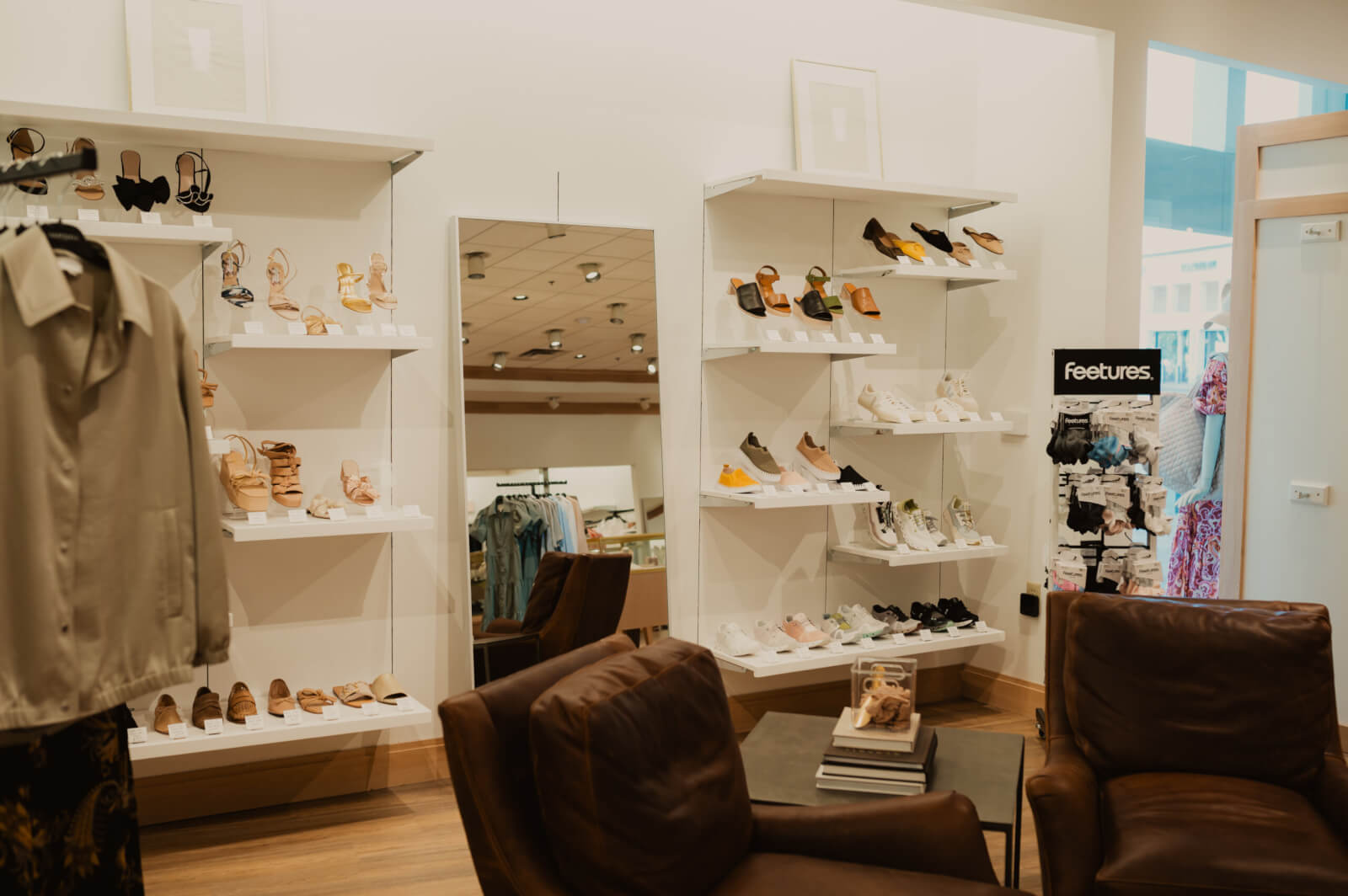 A shoe store interior with shelves displaying various footwear styles, two brown chairs, a mirror, and a clothing rack in the background at Oak Hall.