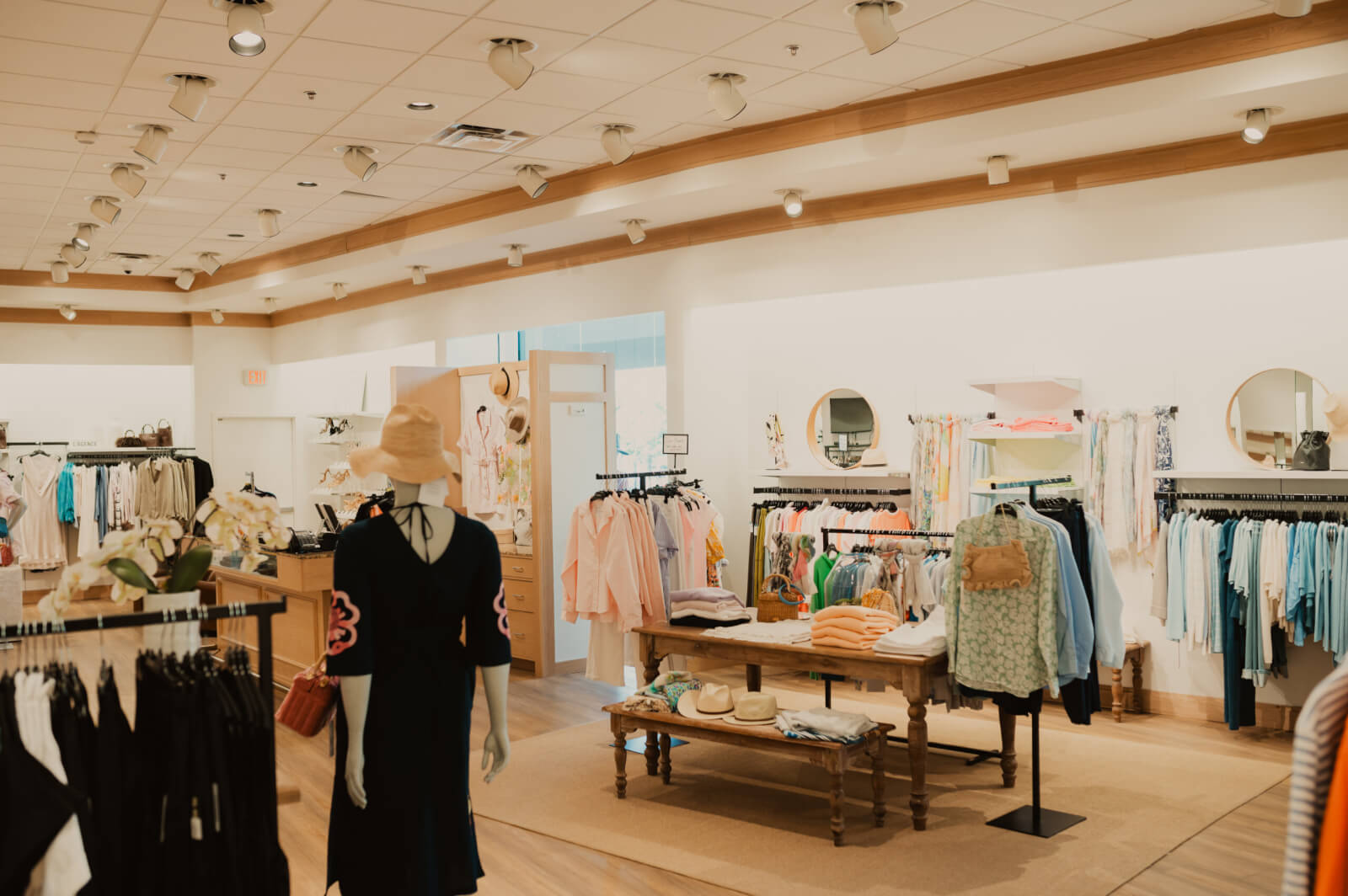 Interior of Oak Hall, a brightly lit clothing store featuring neatly arranged racks, shelves with folded clothes, hats, and a mannequin wearing a dress and hat.