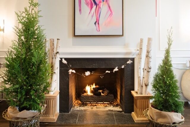 Leland Cypress trees and pretty logs flank the fireplace. Note the added garland connecting the logs! And, how fun is the added pop of color from the modern art?