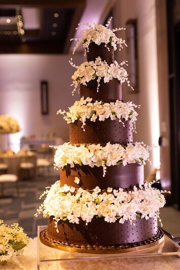Tall, multi-tiered chocolate wedding cake adorned with white floral decorations.