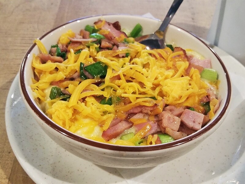 A bowl of grits loaded with cheese, ham, and scallions at Urban Standard