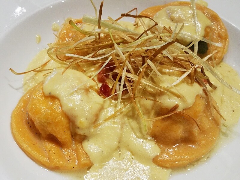 House-made tomato-infused-pasta ravioli, stuffed with lobster, shiitake mushrooms and ricotta with a drawn sage-butter and sweet-corn-cream puree, topped with carmelized leeks.