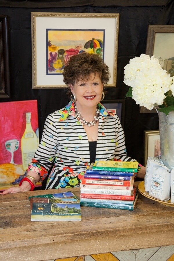 Daisy stands behind a stack of the many cookbooks she's penned since 1978. Fourteen to be exact!