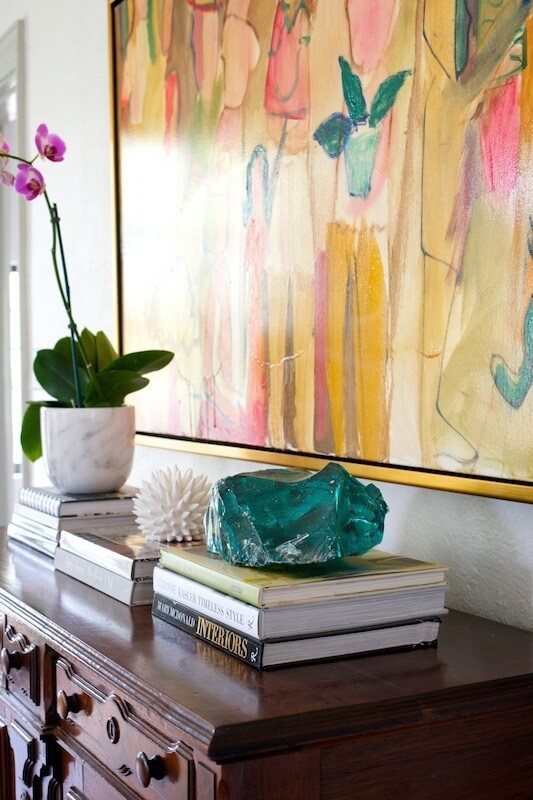Simple stacks of books topped with interesting accessories allow the artwork to remain the focal point while also making the space feel lived-in.