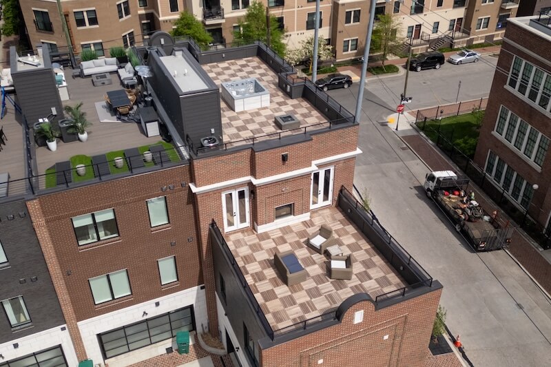 Aerial view of a modern urban apartment building with a rooftop terrace featuring patio furniture and a chessboard design floor.