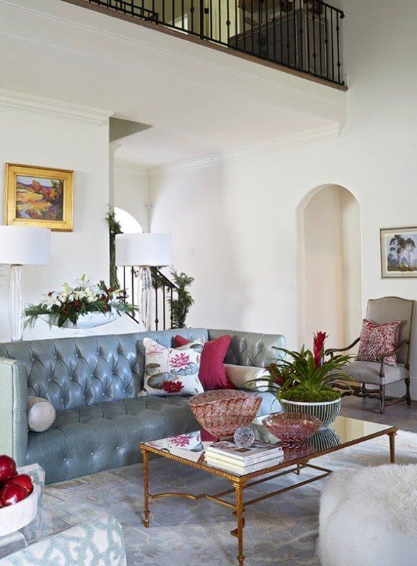 The open, airy living space opens up to a high ceiling accented with wooden beams and a second-floor balcony, which creates a space that is comfortable and inviting, while also elegant and grand. The seating in the space is grouped in a close arrangement atop a lovely Oushak rug, allowing for intimate conversation and functional movement through the living room. Soft neutrals throughout the room are broken up with gold details and pops of red, all coming together to create a tranquil, soothing space.
