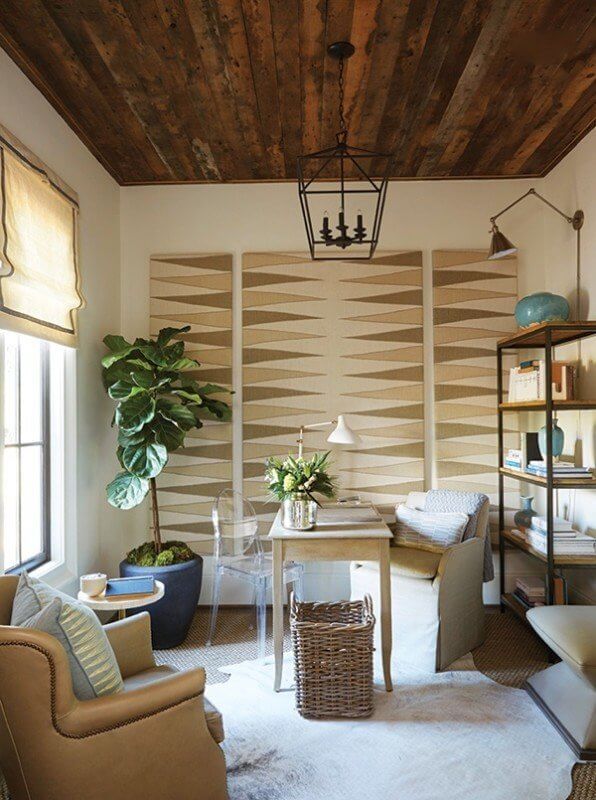 The home office area is teeming with layers of energy and creative inspiration. Varied neutrals are accented by serene shades of blue and green, and a sisal rug is layered with a soft hide underfoot at the desk area. Large windows bathe the space with plenty of light for the charming Fiddle Leaf Fig Tree tucked into the corner of the room. All of these details simply accent the star of the space, the graphic fabric panels on the wall, crafted from Mary McDonald Schumacher fabric.
