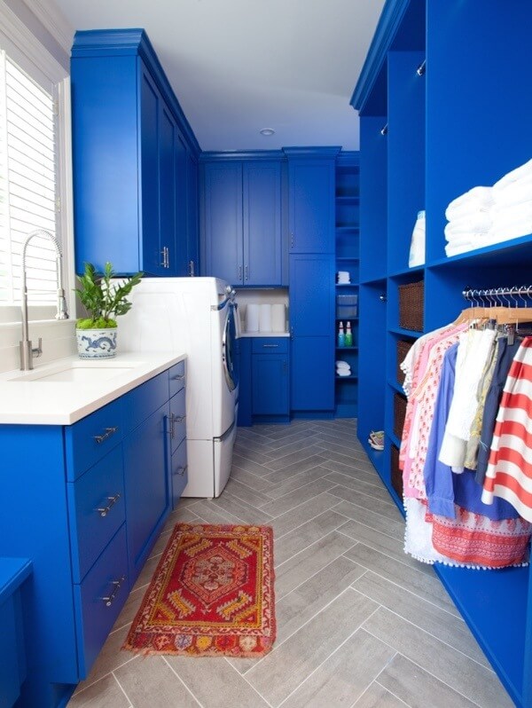 Laundry room cabinets wear the same vivid blue as the butlers pantry, but with muted stone floors as contrast.