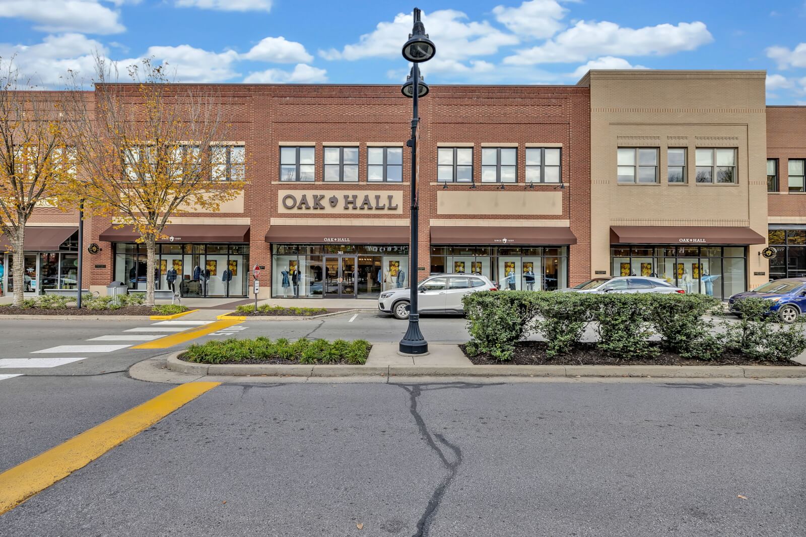 Street view of the two-story brick Oak Hall building, with parked cars, trees, and a crosswalk in front under a partly cloudy sky.