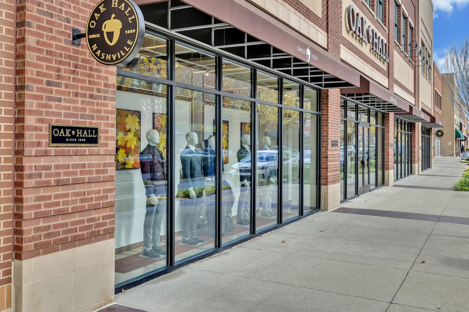 Street view of Oak Hall in Nashville features large glass windows showcasing mannequins dressed in stylish clothing and autumn-themed decorations.