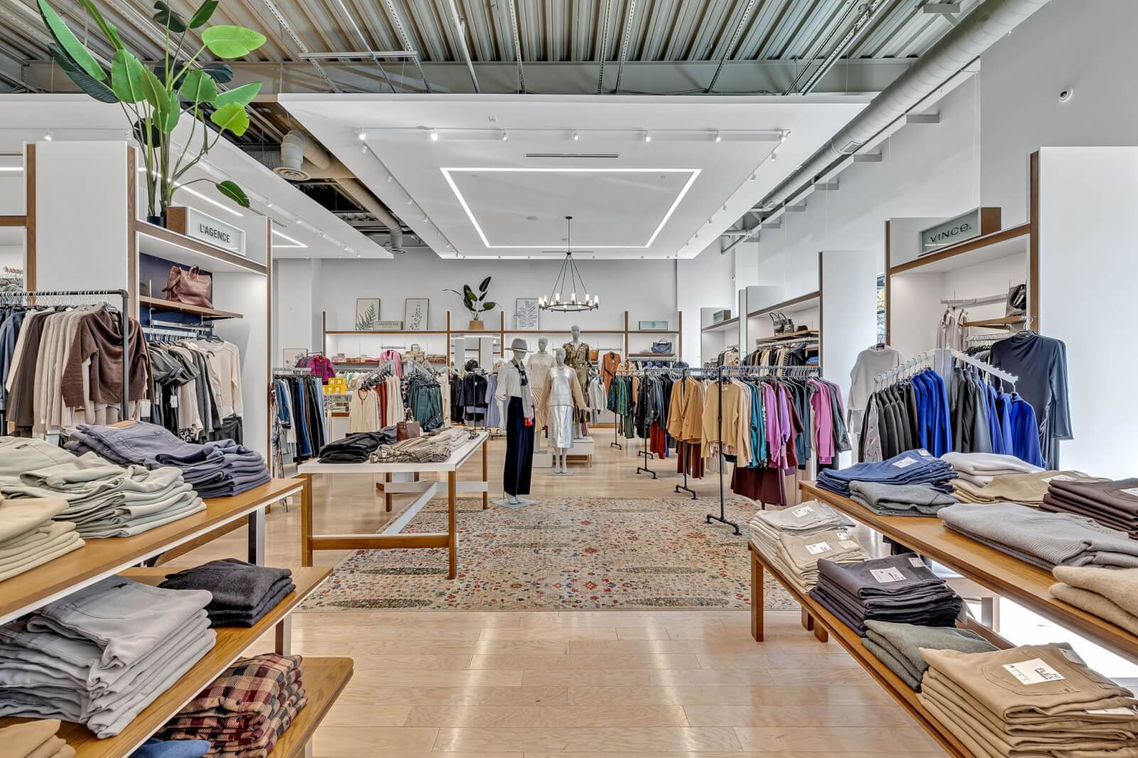 Clothing store interior with neatly arranged racks of clothes, folded apparel on tables, mannequins in the center, and bright lighting creates a welcoming atmosphere at Oak Hall.
