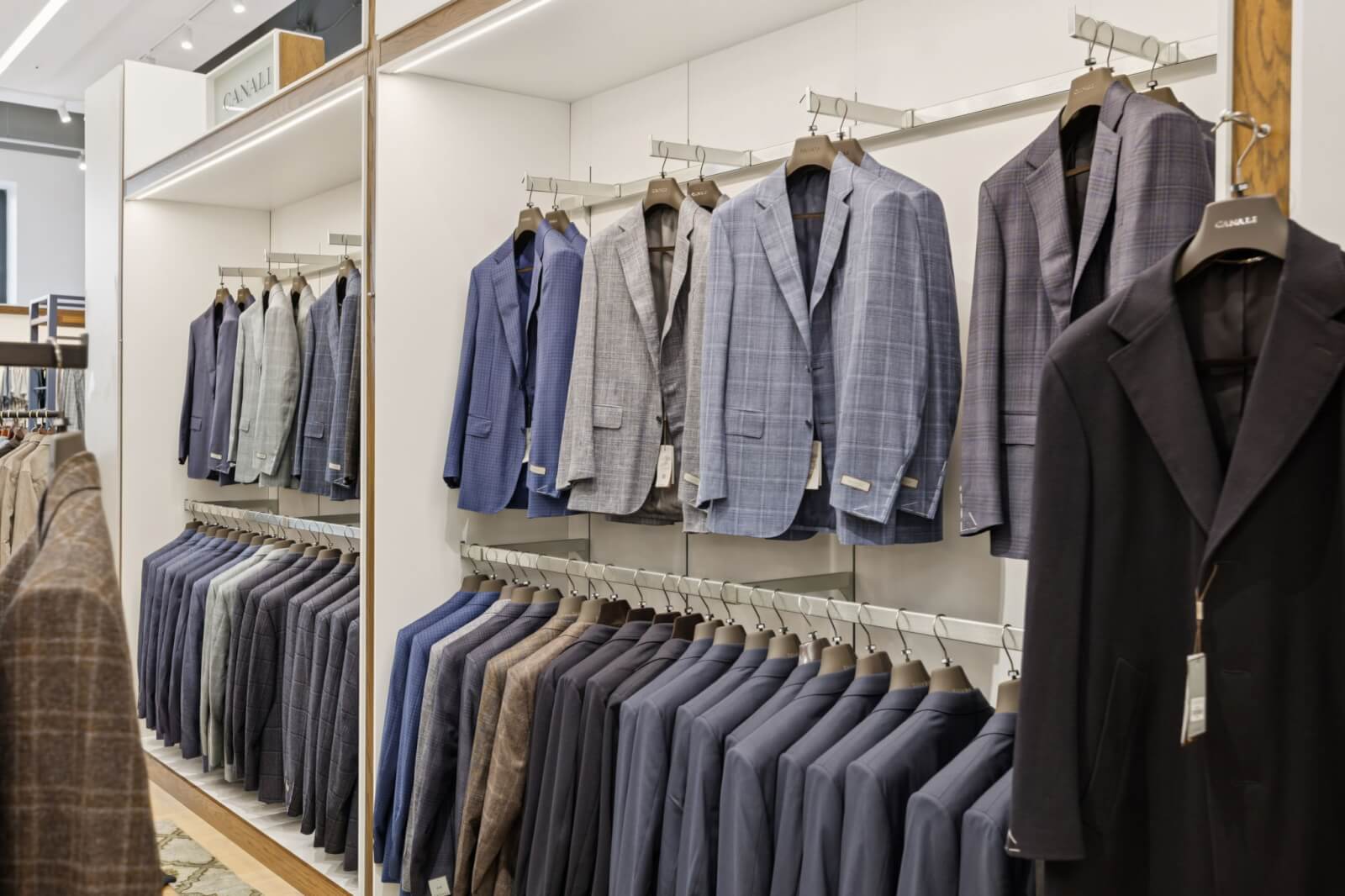 A clothing store display at Oak Hall with suits and blazers in various shades of blue, gray, and brown hanging neatly on racks.