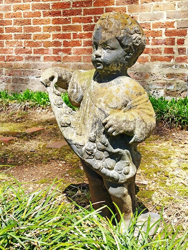 An angelic statue curtsies among the bricks and moss.