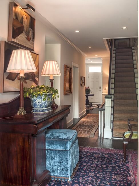 The second floor foyer showcases an Empire sideboard from the 1840's that was made in Savannah. “I had the ottoman custom made to fit underneath it,” says Brandon. “I love the great pop of color with the rug.”  Artwork is by a SCAD (scad.edu) student.