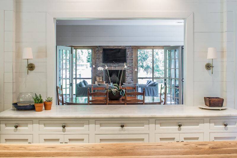A pass-through from the kitchen to the home's casual interior dining area opens to the porch and makes for effortless entertaining. Image| Julie Wage Ross