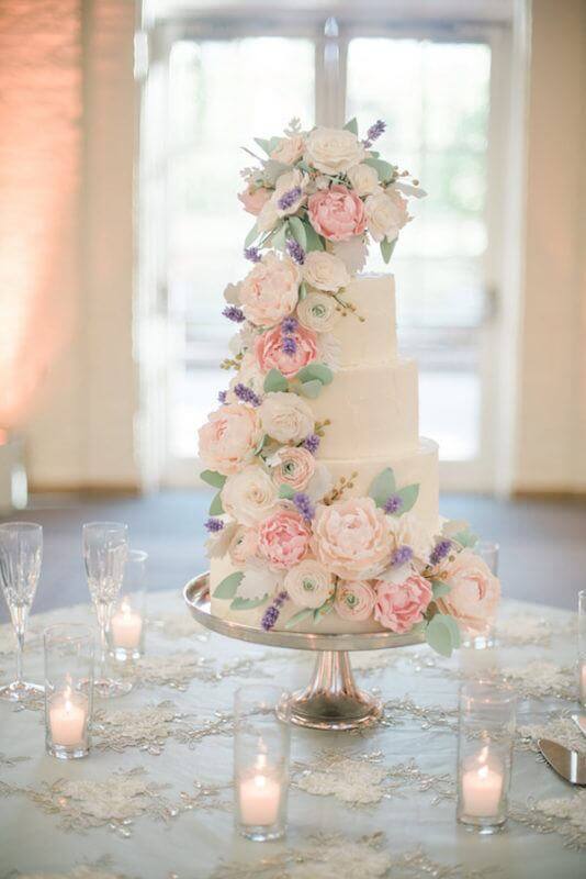 The cake had two flavors: chocolate cake with raspberry icing and vanilla cake with strawberry icing. It was beautifully decorated with realistic sugar flowers cascading and topped with a silver bowl filled with sugar flowers, the same as Sarah’s parents and on their wedding cake in 1975. The four tiered cake stood underneath the floral chandelier on a table with lace overlay and tea lights.