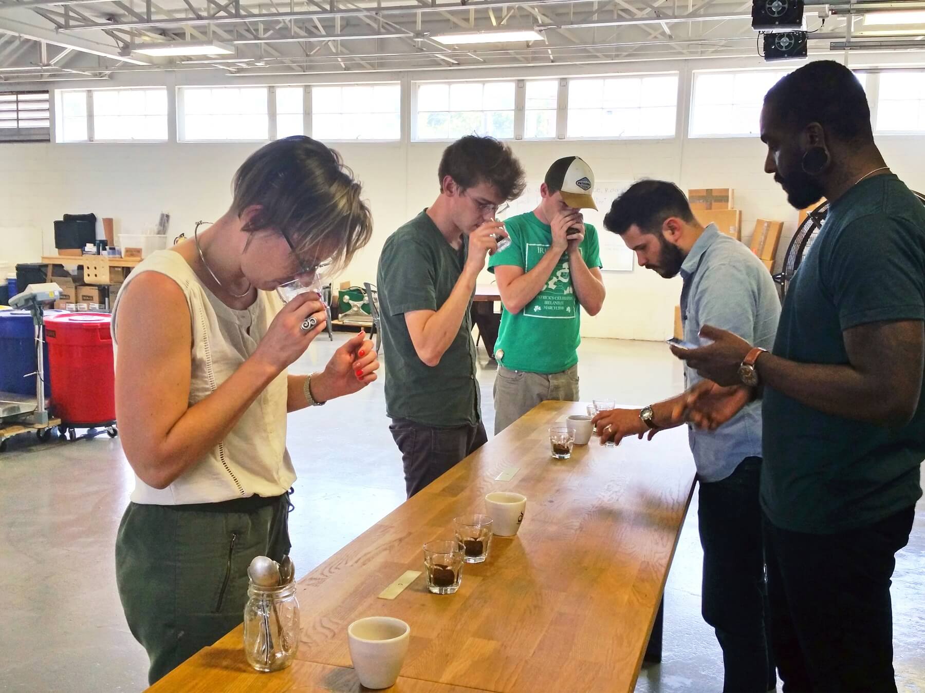 The cupping team sniffs and takes notes on their phones.
