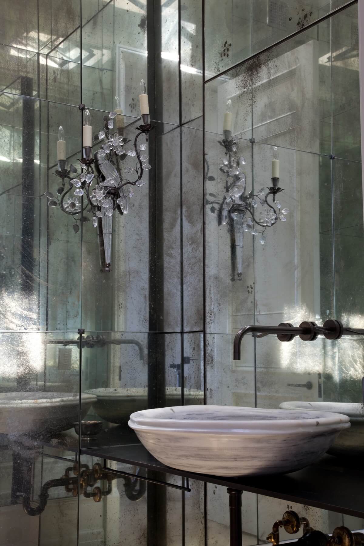 This striking powder room with its antique mirrored walls, pair of iron and crystal bird sconces and antique Turkish stone sink is truly one of a kind. Image: Miller Mobley