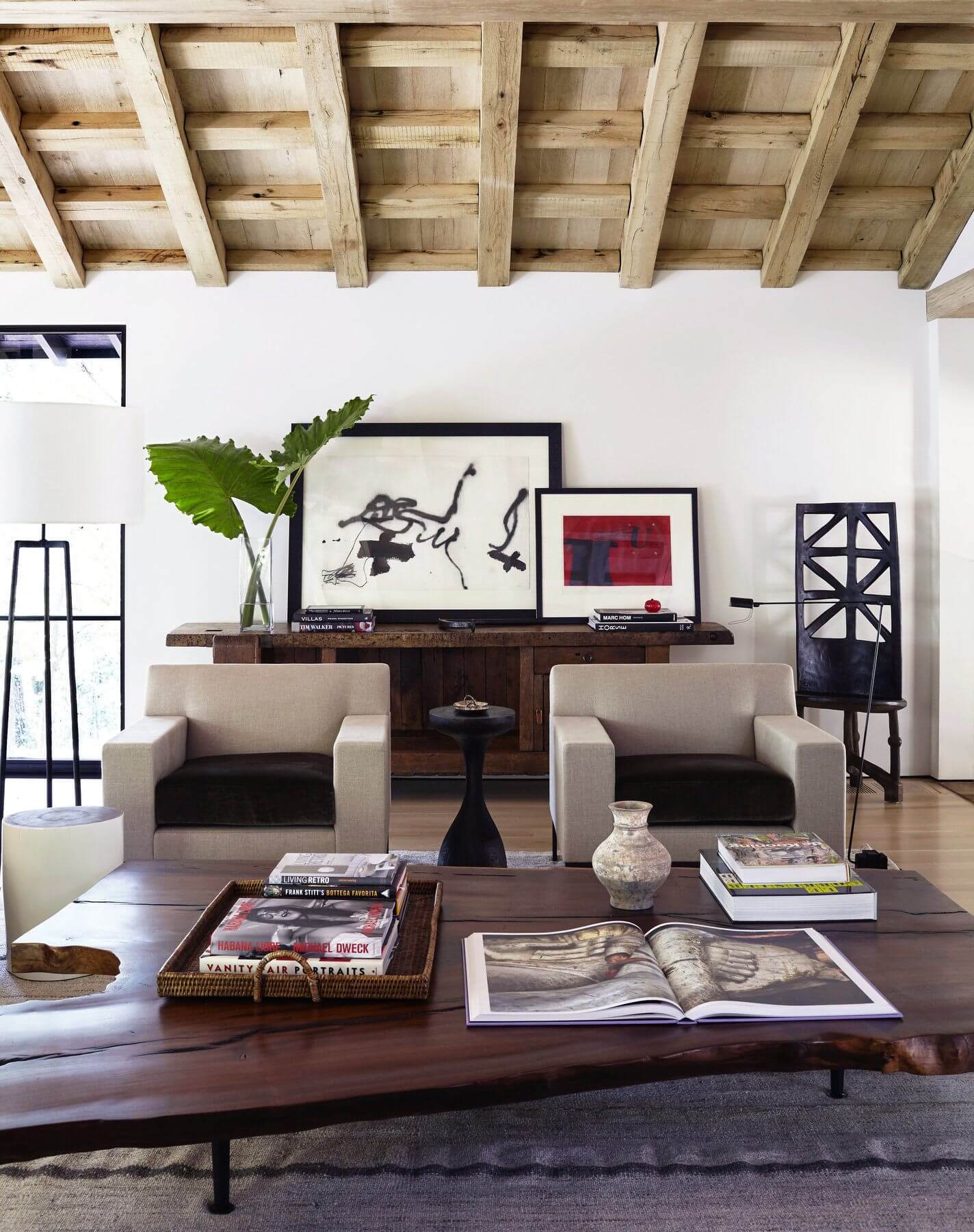 The family room is anchored by an asymmetrical custom walnut coffee table beside a sleek pair of Christian Liaigre armchairs atop a vintage kelim rug. Client's own antique oak French work table creates the base for a beautiful sideboard display, which includes an African high-back chair. Image: Jean Allsopp