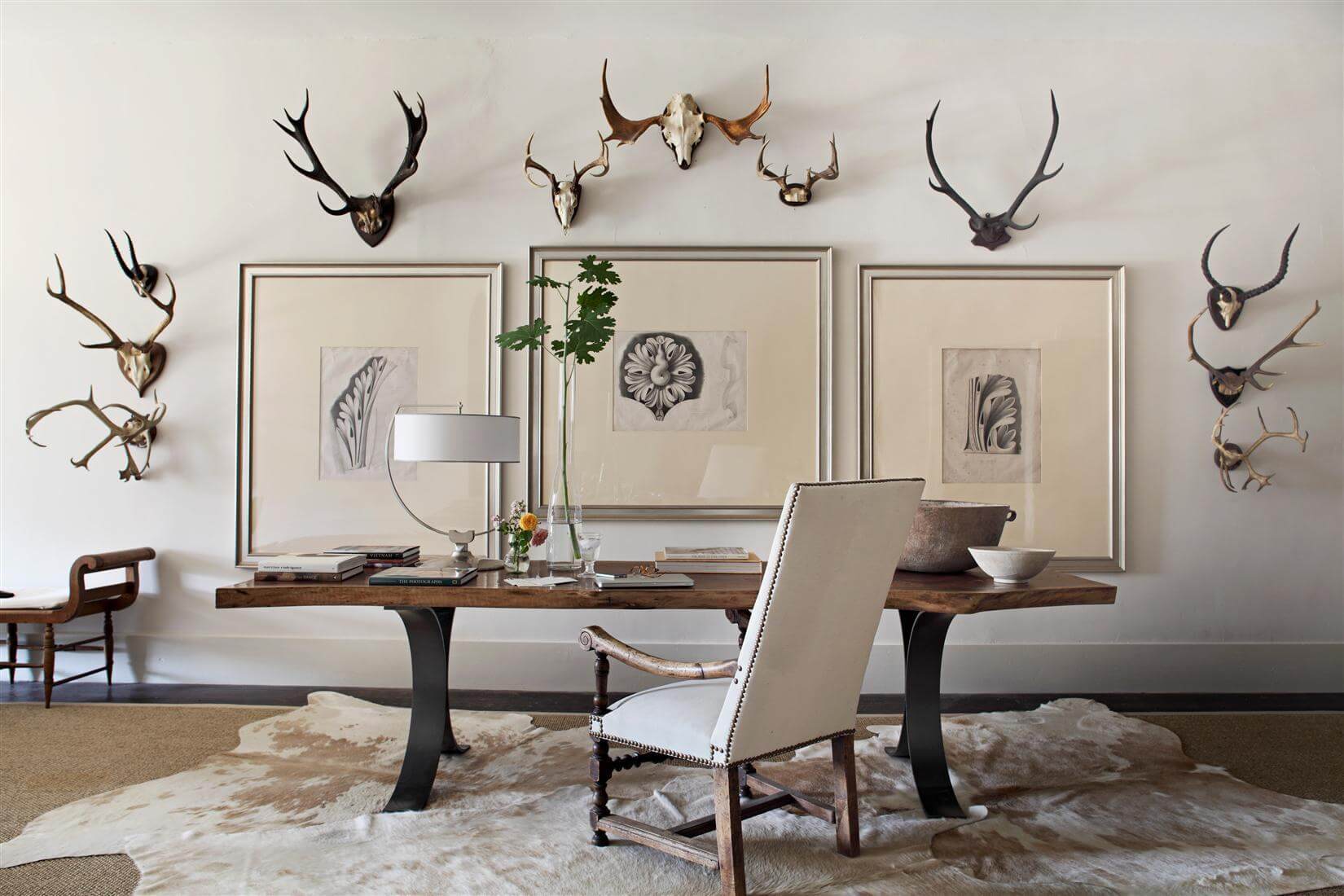 The client's own collection of vintage European antlers gets its day in the sun beside antique prints of Greek Revival plaster designs in this upstairs hallway vignette, where an 18th Century Louis XIV-style armchair flanks a custom walnut table by Michael Morrow. Image: William Abranowicz 
