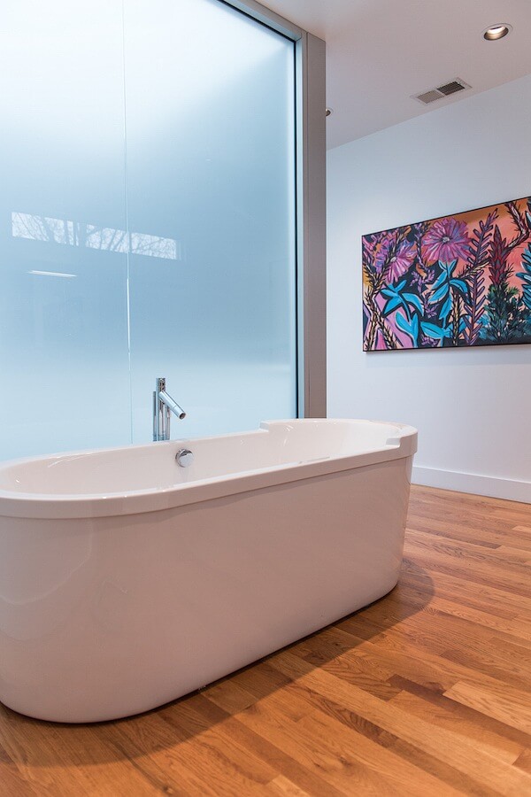 Soaking tub is against an opaque glass wall, which allows light.