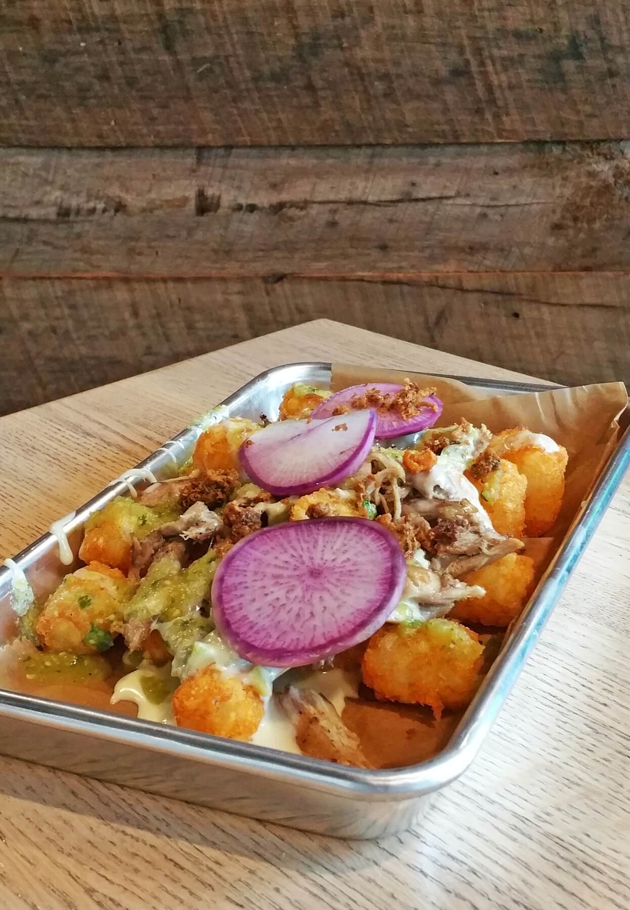 The "Duck Totchos" marry the concept of tater tots with nachos. The dish starts with a base of house made tater tots and is topped with green chile queso, duck confit, salsa verde, radish and cracklin's. The "Duck Totchos" marry the concept of tater tots with nachos. The dish starts with a base of house made tater tots and is topped with green chile queso, duck confit, salsa verde, radish and cracklin's.