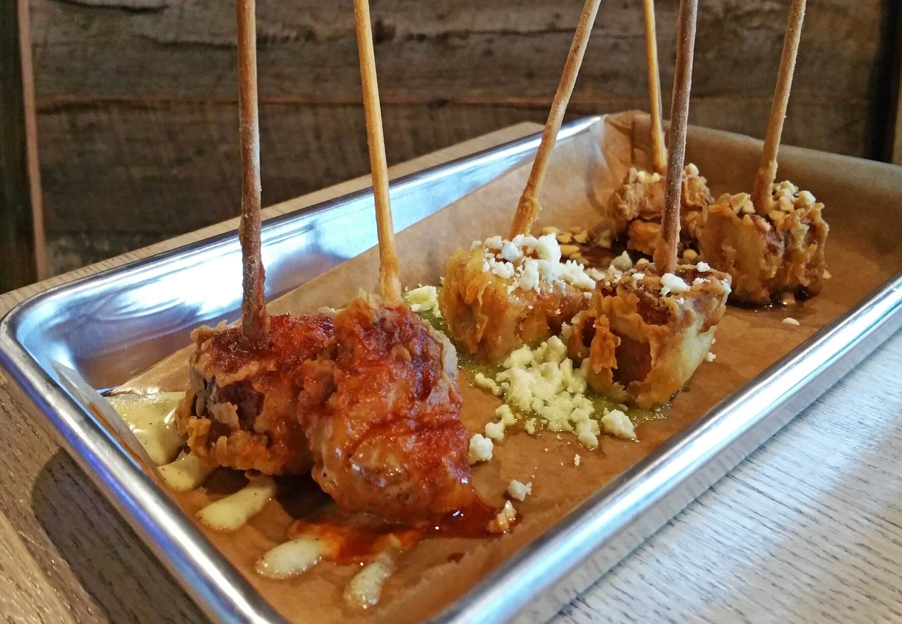 The Pork Belly Lollipops features Red Hills Mild Brown-braised pork belly with a crispy finish, served three ways: Topped with SoHo maple sauce and crushed peanuts; topped with salsa verde and cotija cheese; and topped with SoHo and white barbecue sauce. The Pork Belly Lollipops features Red Hills Mild Brown-braised pork belly with a crispy finish, served three ways: Topped with SoHo maple sauce and crushed peanuts; topped with salsa verde and cotija cheese; and topped with SoHo and white barbecue sauce.