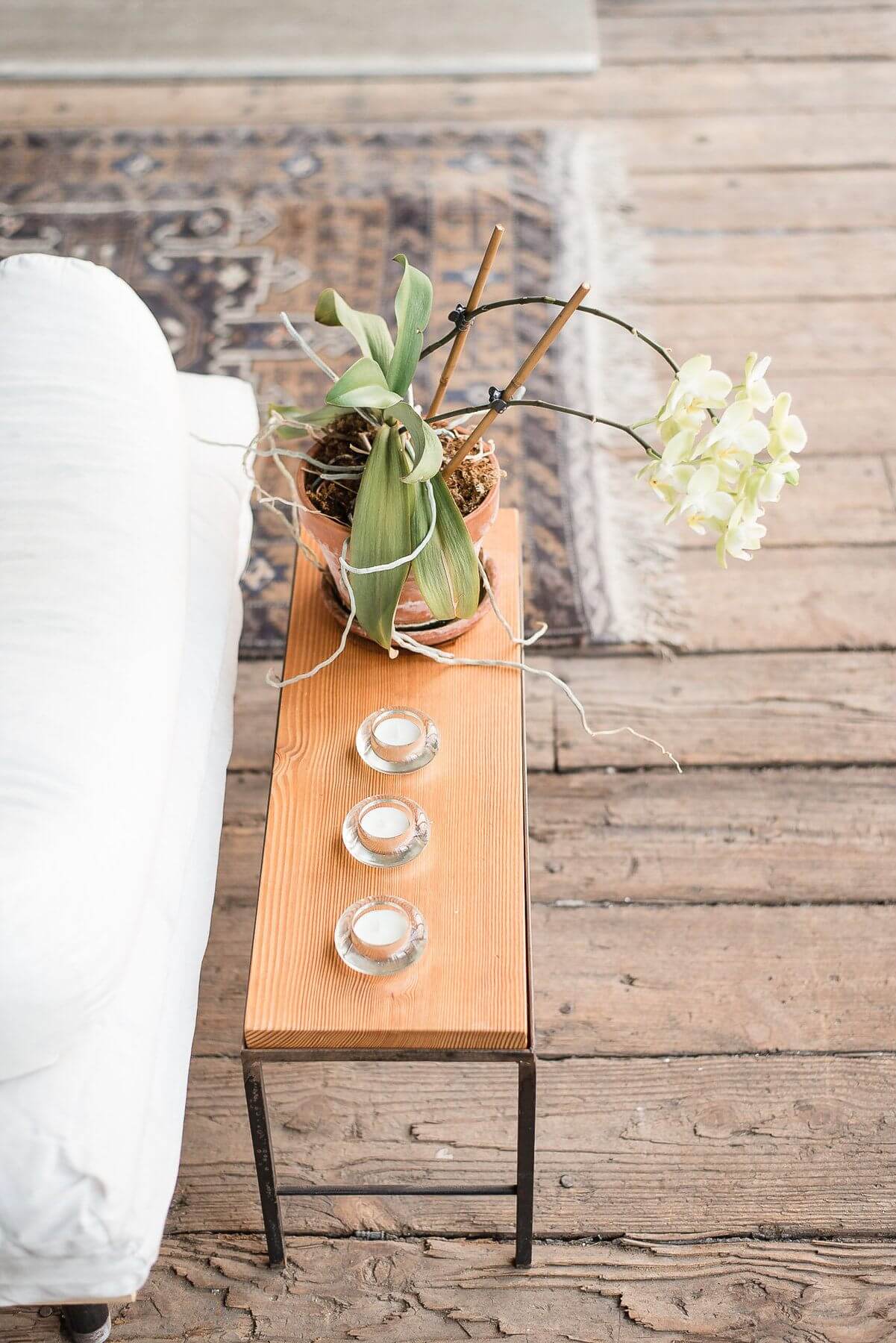 A small, modern side table atop the rugged original wood flooring houses a sleep trio of tea lights and a potted orchid. A small, modern side table atop the rugged original wood flooring houses a sleep trio of tea lights and a potted orchid.