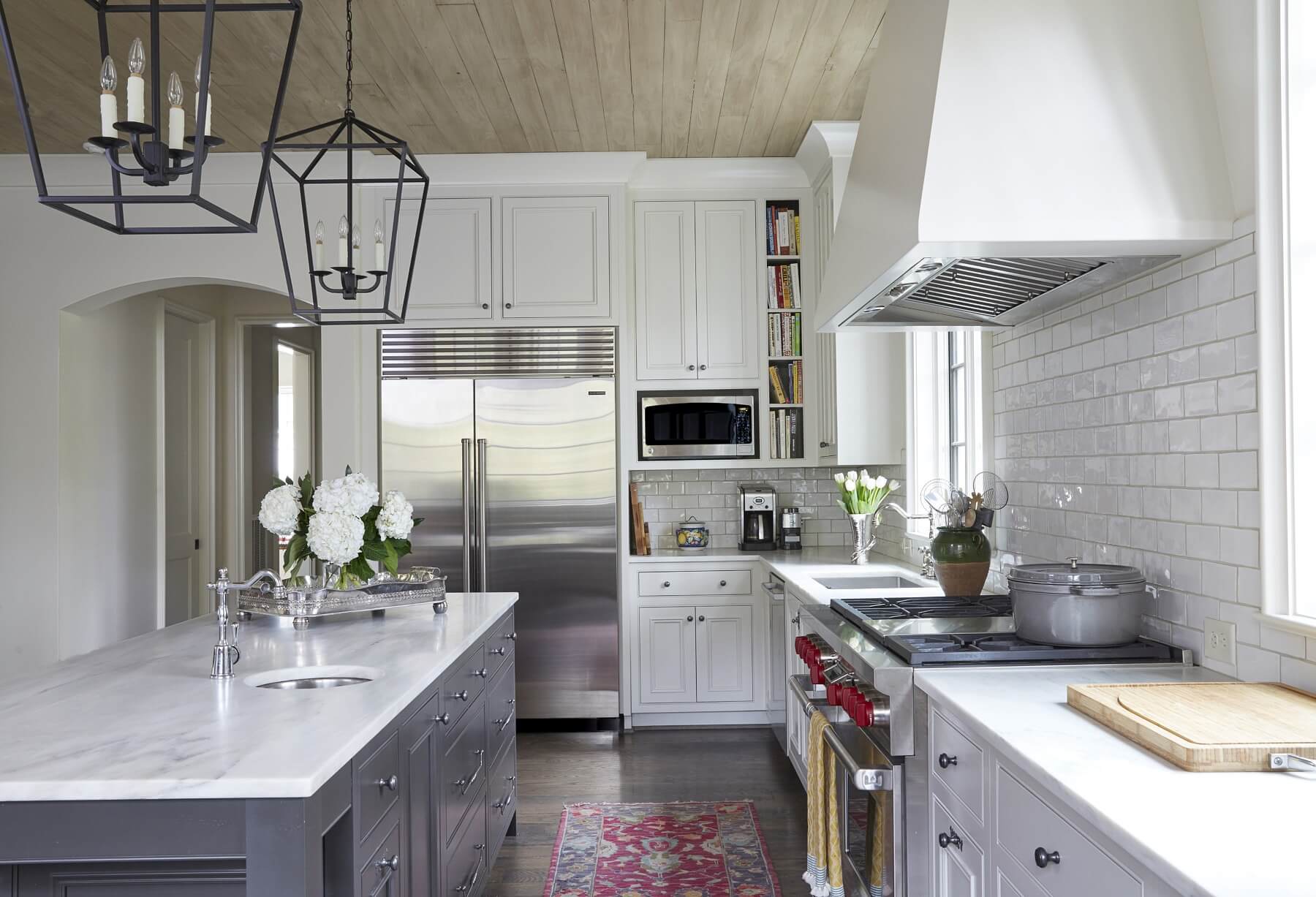 Crisp white elements are complemented by the warmth of the rug, the calming blue island cabinetry and the wooden ceiling.