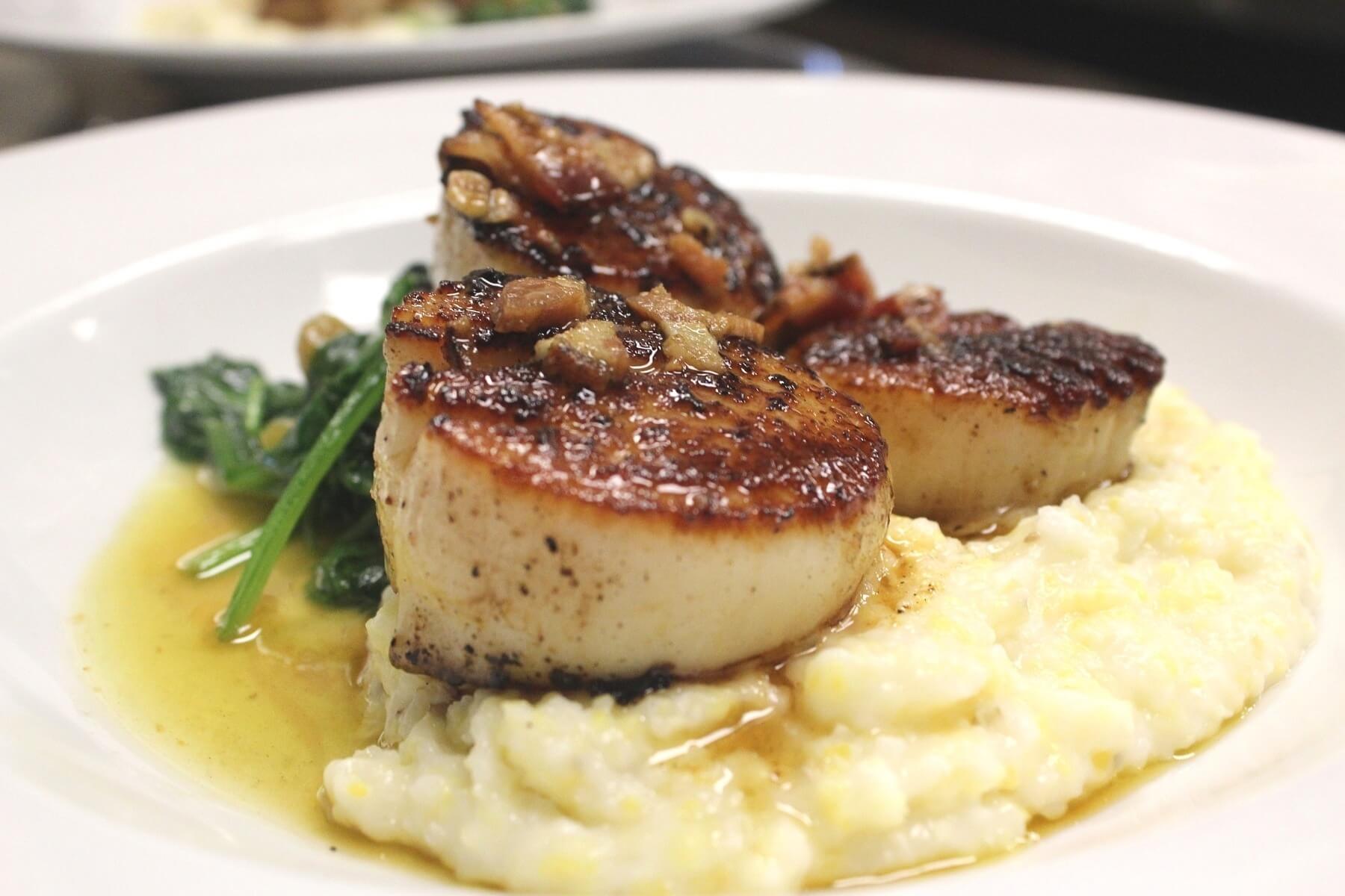 Pan-seared jumbo scallops atop grits and Catalan spinach, drizzled in Nueske's bacon vinaigrette