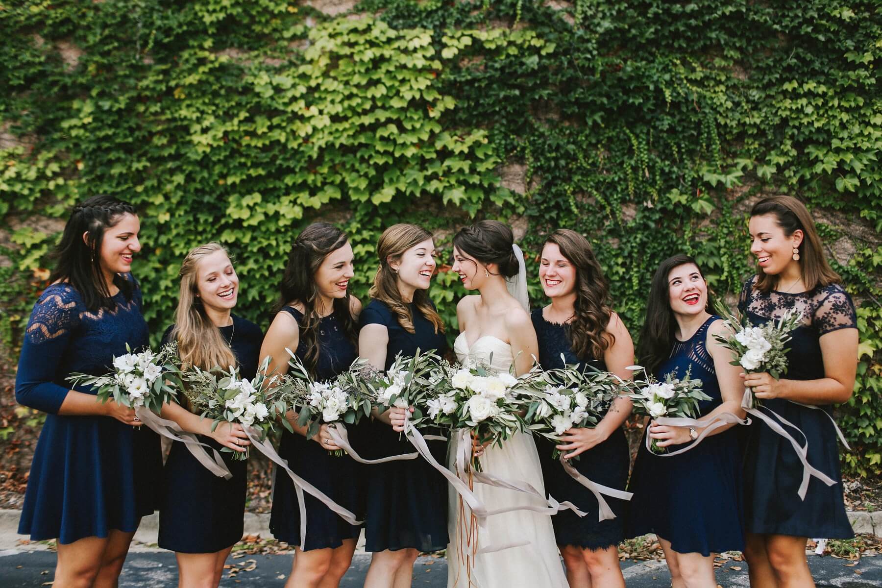 The bridesmaids wore navy dresses of their choosing and carried whimsical bouquets of greenery with touches of soft white blooms, tied up with long strands of gray ribbon.
