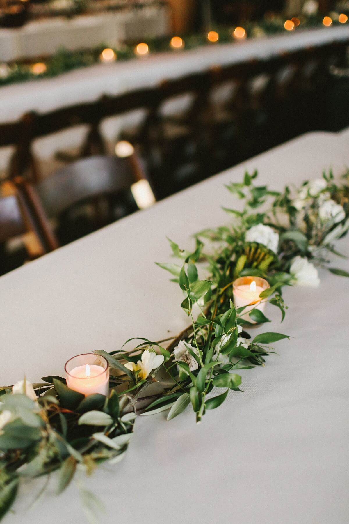 Simple white linens and lines of greenery dotted with florals and glowing tea light candles created the perfect romantic feel in the space.
