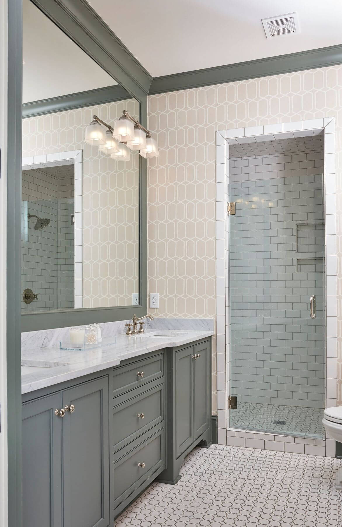 A subtle lattice pattern on the wall is contrasted with grey-green paint on cabinets and millwork in this charming bathroom.