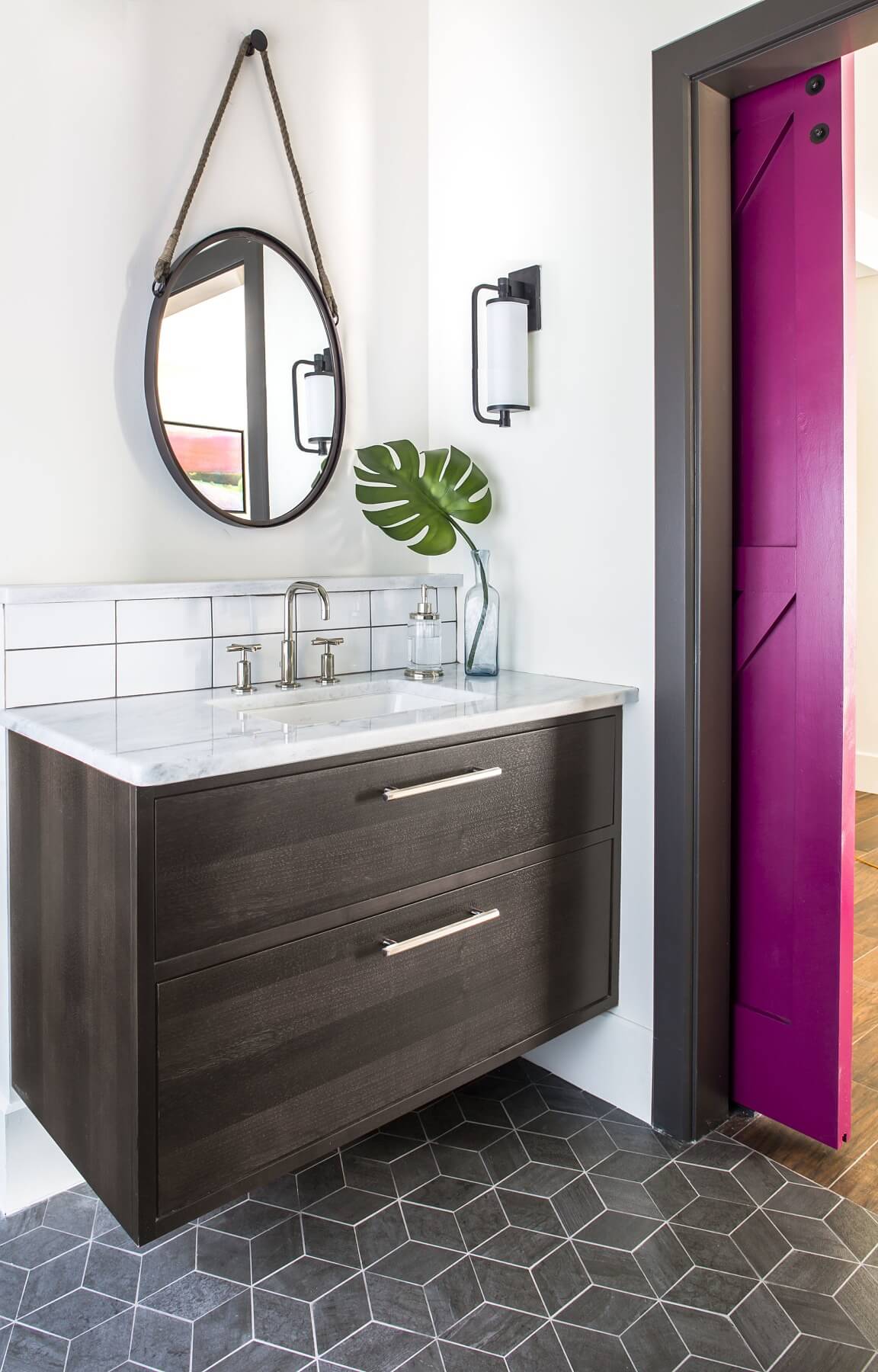 A floating vanity, geometric tile floor, and fuchsia barn door distinguish this lively bathroom.