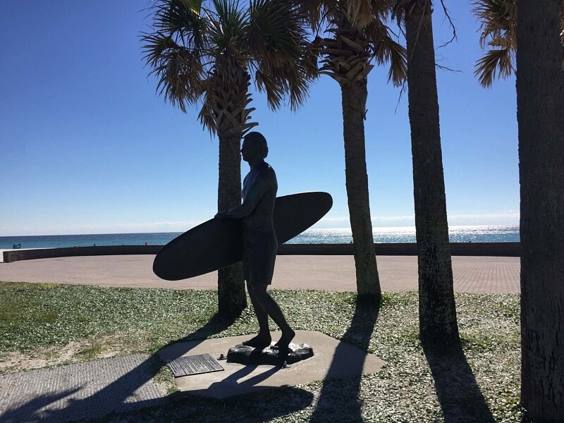 A statue honoring a famous local surfer is located near the fishing pier.