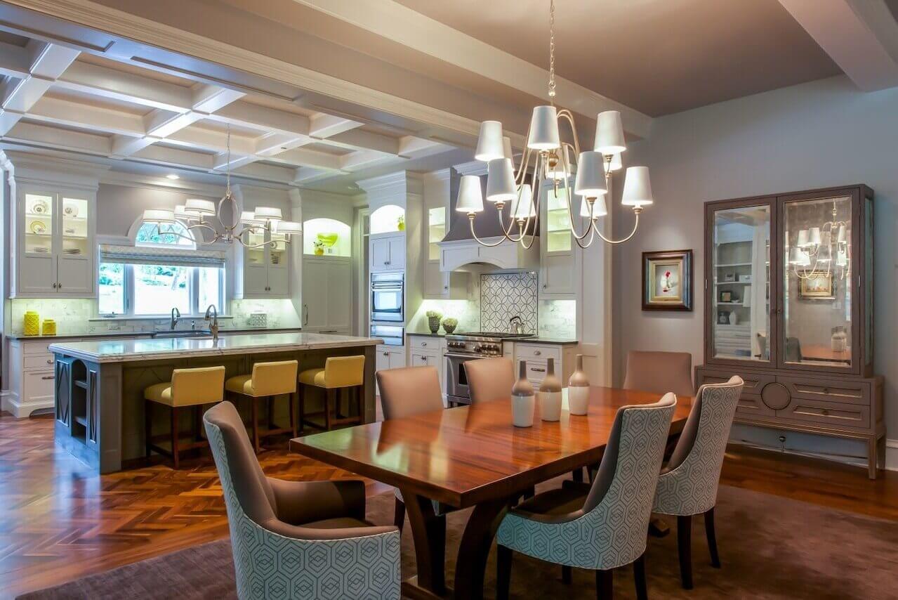 The spacious first floor also opens to the chic gray kitchen, with its marble and quartz countertops. Floors are natural black walnut. <a href="https://www.kravet.com/" target="_blank">Kravet</a> fabric covers the custom barstools at the spacious island. The adjacent keeping room continues the gray and yellow theme.
