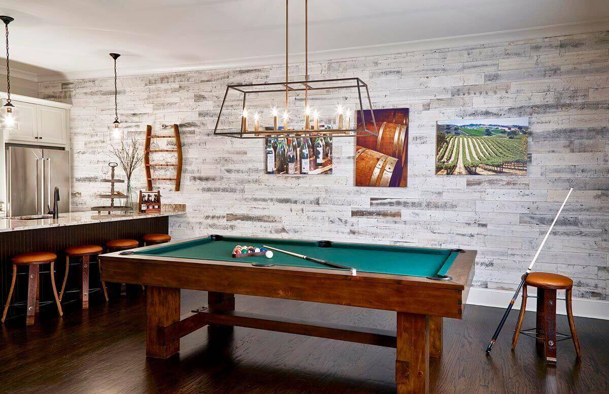 The husband wanted the billiards room to look like his favorite restaurant in Roswell that has a ‘wine cellar’ feeling, so the designers ordered Stikwood https://www.stikwood.com panels applied to the walls. Continuing the rustic look,   bar stools have legs made from wine barrels.