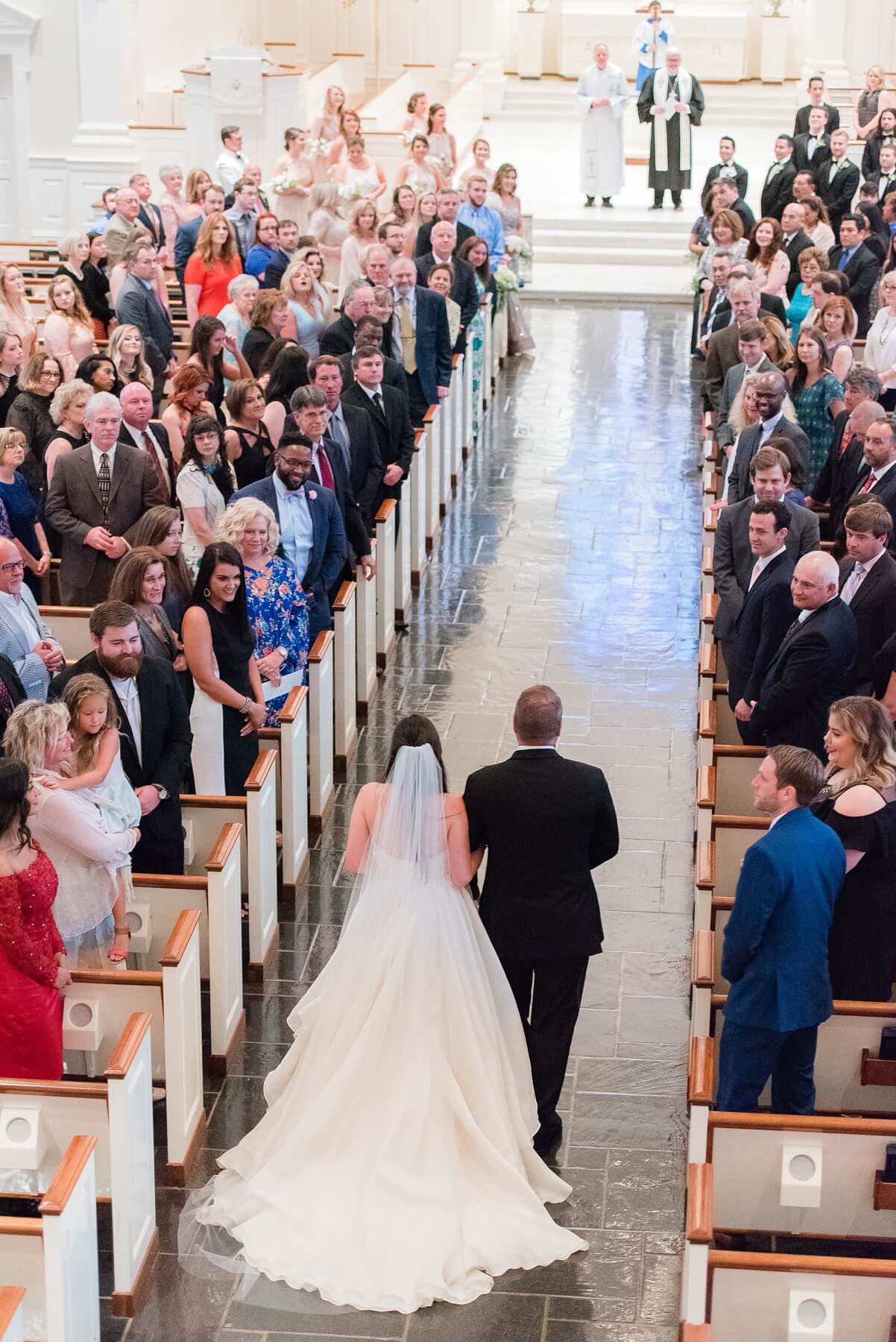 On her father’s arm, the bride walks down the aisle toward her groom.
