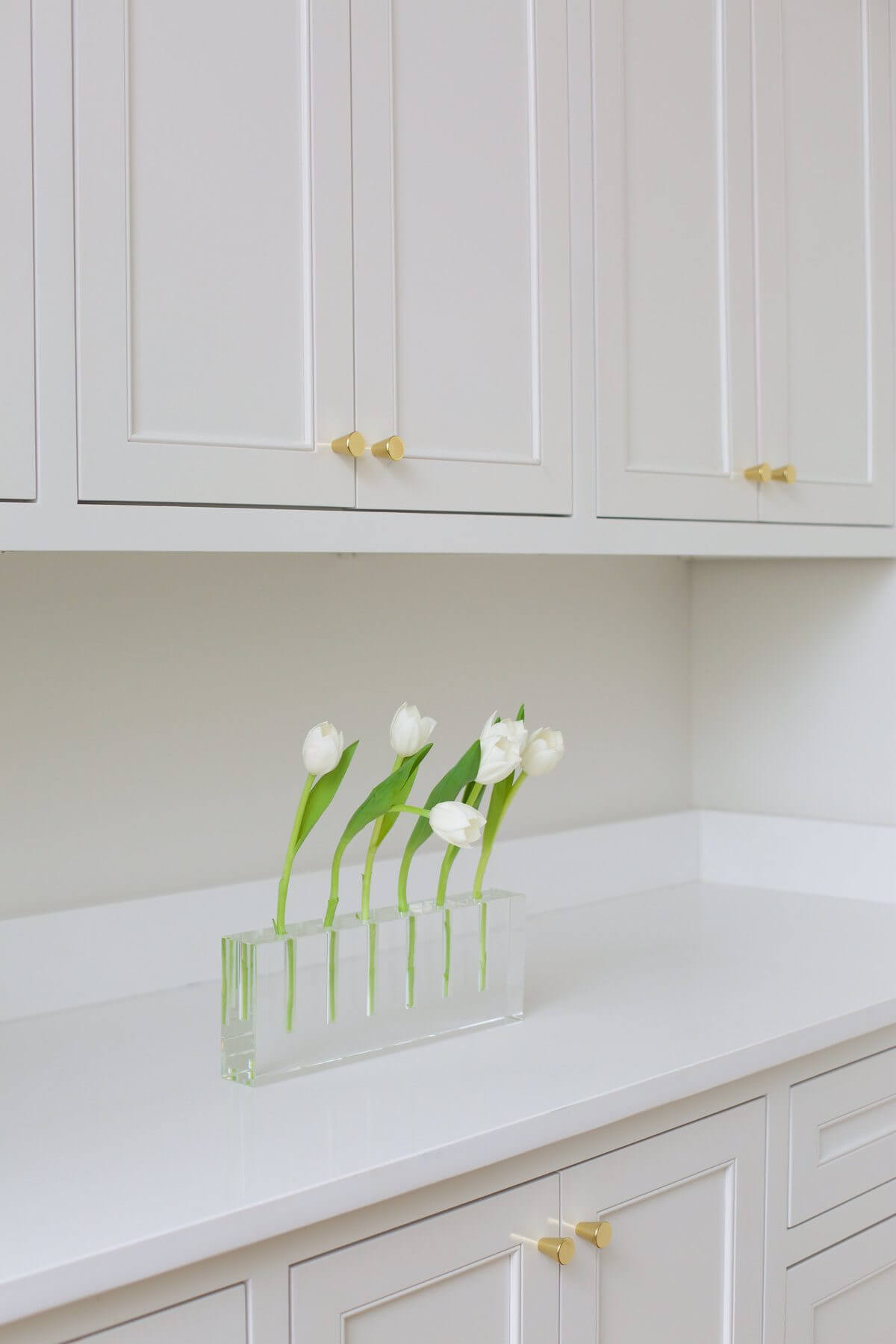 The all-white kitchen features gold accents with the hardware and light fixtures for a thoroughly minimalist beauty. AG Designs