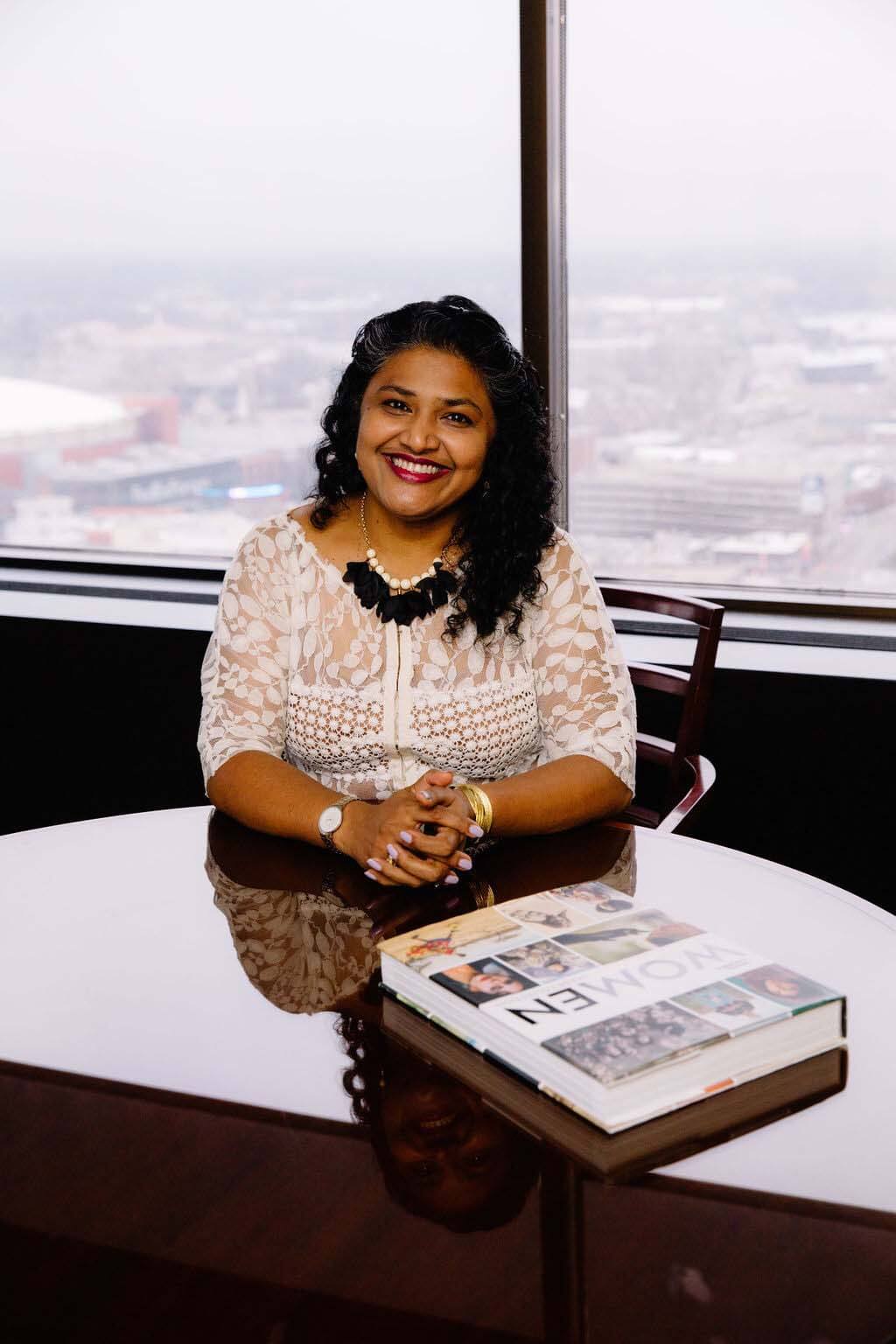 In addition to serving as co-founder and president of Powers Hill Design, Nisha also serves as the co-chair for the Women's Foundation for a Greater Memphis. Nisha Powers sitting at a table with a book.