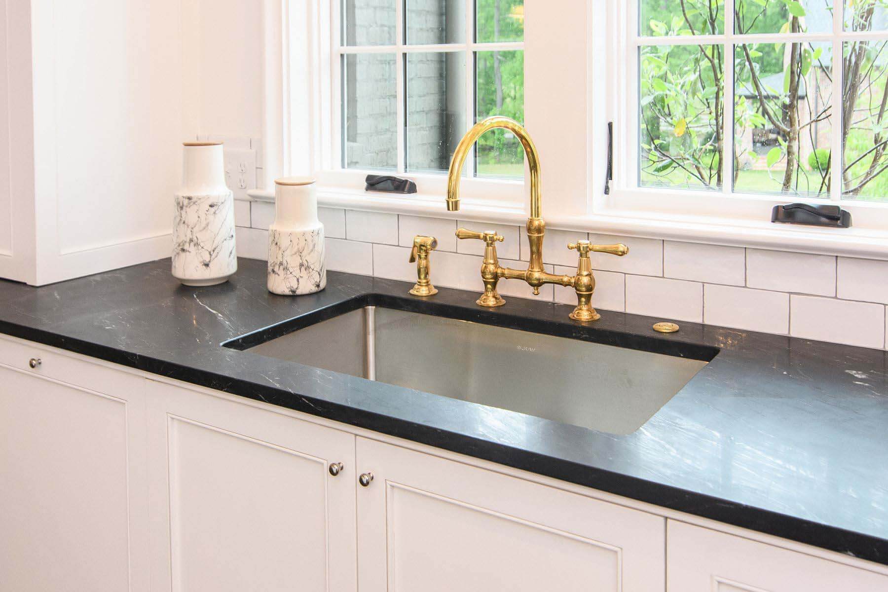 A favorite design element is the unlacquered brass faucet. It pops against the black countertops and white tile backsplash. Woody O’Neal Farmhouse sink with brass faucet
